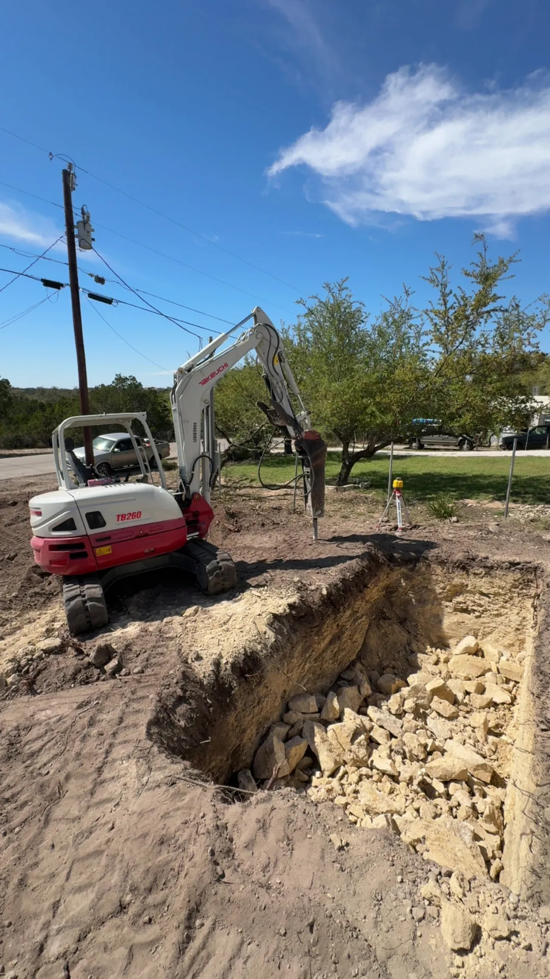 Excavator with hydraulic hammer breaking rock for a tank excavation